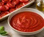 Bol de sauce tomate rouge et lisse, entouré de tomates rôties, d'ail et de basilic