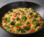 Poêle sombre garnie de riz sauté, morceaux d’œuf, épinards, brocoli, poivron rouge, carotte et pois gourmands